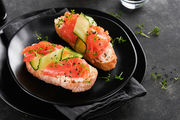 Sandwiches. Salmon toast with cream cheese, cucumber, black sesame and microgreens on black background. Seafood. Healthy food. Photography in low key. Top view.