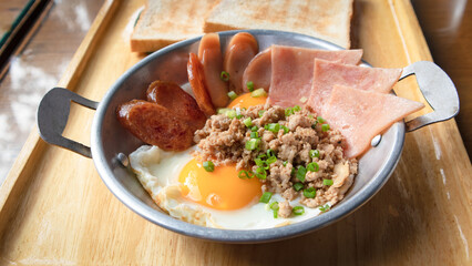 Fried eggs in a small pan with ham, minced pork, spring onion and chinese sausages on wood tray. Popular Thai Breakfast called Kai Kata