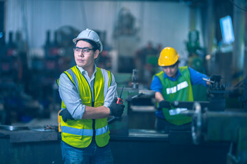 The yellow safety helmet engineer standing and looking the future and hold the two way radio or walkie-talkie in front of machinery and other worker doing sone work