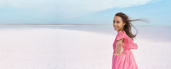 Panoramic banner image beautiful landscape with elegant smiling woman, giving hand to camera like follow me at salt flats beach of pink lake. - 509177384