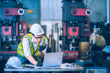 The white safety helmet working with laptop and order thought a walkie talkie in front of machinery