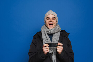 Young white man wearing winter clothes using cellphone and laughing