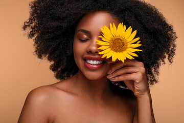 Happy African American model covering eye with sunflower