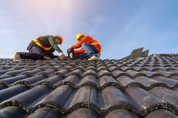 Teamwork of Asian roofer workers in protective uniform wear and gloves, using air or pneumatic nail gun and installing Concrete Roof Tiles on top of the new roof, building under construction. - obrazy, fototapety, plakaty