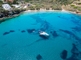 Aerial view of the beautiful Lotos Beach next to Kini bay at Syros island, Greece, with a sailboat moored over turquoise sea