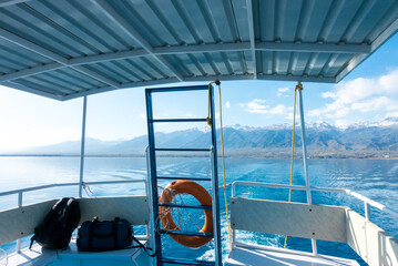 Ship's stern, lifeline. Footprint on the water from the boat. Blue water and mountains on the...