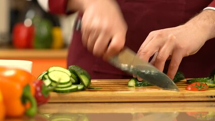 Chef chopping fresh, green 
cucumber. Close view man cutting fresh cucumber with sharp knife on cutting board. Preparing vegetable for cooking for salad. Healthy Food Concept.