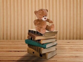 Cute brown teddy bear and stacked books on a shelf.