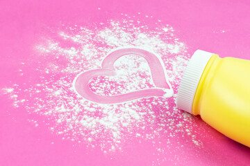 Children's background. A painted heart on a baby's white powder (talc) under a diaper and a yellow jar on a bright pink background close up.