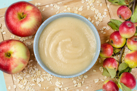 Oatmeal porridge for the baby from ground cereals in a blue bowl, red ripe apples on a wooden board close-up. The first complementary food of a child, baby nutrition.