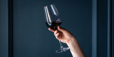 A glass of red wine in a female hand on a blue background.