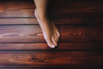Left female feet on a brown wooden floor background close up. Foot hygiene concept.