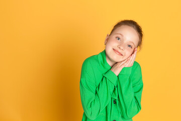 Portrait of a beautiful smiling little girl with long hair. A girl in a green suit on a yellow background in the studio shows emotions. place for text