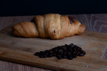 Croissant on baking paper, on wooden table, dark background, morning breakfast, coffe beans, side view