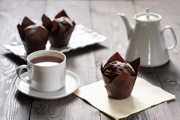 A cup of tea and dark cupcakes on a wooden table. The texture of the wood is visible, there is a white teapot. Food. Lifestyle.