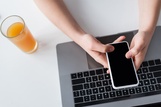 top view of cropped woman using smartphone with blank screen near laptop and glass of orange juice.