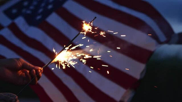 Happy 4th of July Independence Day, Hand holding Sparkler fireworks USA celebration with American flag waving nature outdoor background. Concept Independence Day,Fireworks,Sparkler,Memorial,Veterans