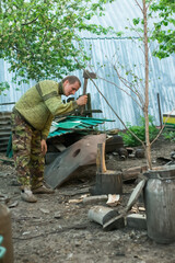 A man in military uniform is chopping wood. Sunny day in the countryside.