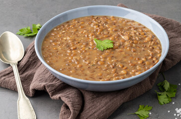 Lentil soup in a bowl with seasoning over stone background