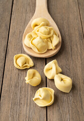 Uncooked cappelletti or tortellini on a spoon over wooden table