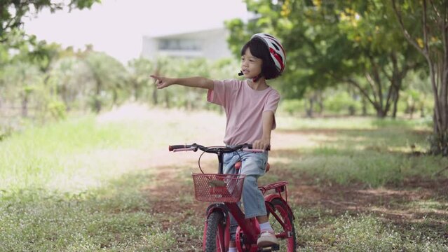 Thai Asian kid girl, aged 4 to 6 years old, looks cute, wears a helmet. and a bicycle She is play riding a bicycle to exercise in the park. It is a fun outdoor activity and learning about nature.