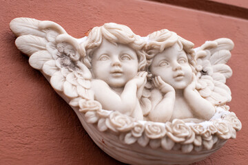 Two baby angels with wings marble sculpture on red wall of building. Close-up, front view.