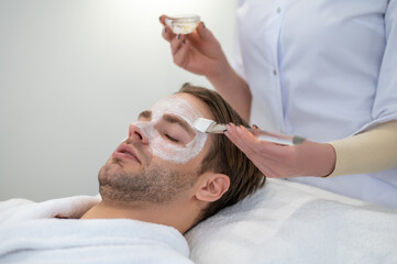 Obraz na płótnie Canvas Beautician putting moisturizing mask on the clients face