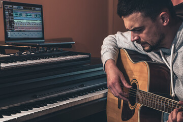Male musician plays the guitar at home in the workplace near the computer.