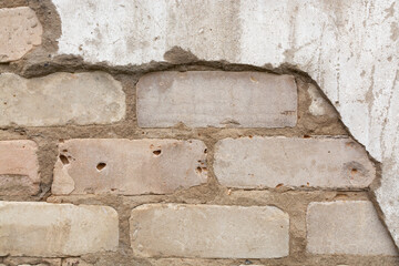 The background (texture) of the destroyed plastered old wall (cement, concrete) from under which the brickwork is visible.