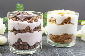 Multi-layered cottage cheese dessert with chocolate corn balls, yogurt and chocolate slices in a glass cup close-up. Romantic breakfast.