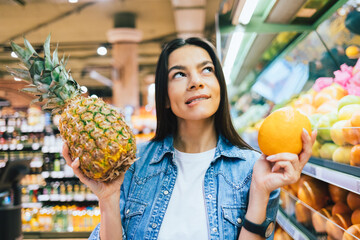 Dreamy young woman choosing goods holding pineapple