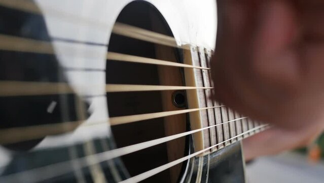 in detail, DOF: the hand of a boy guitarist plays a six-string acoustic guitar in black. The musician's fingers strike the strings while playing the rhythm guitar.