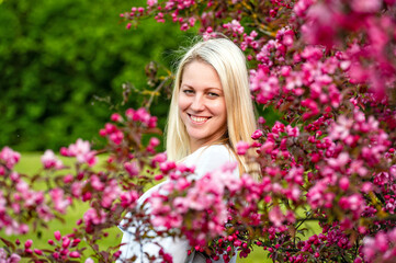 Naklejka premium closeup portrait of a smiling blonde woman in a blossoming garden in spring, selective focus
