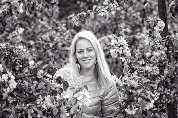 portrait of a smiling blonde woman in a blossoming spring garden, black and white, selective focus