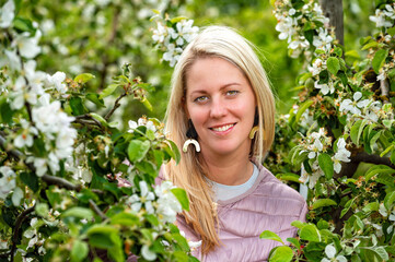 closeup portrait of a smiling blonde woman in a blossoming garden in spring, selective focus