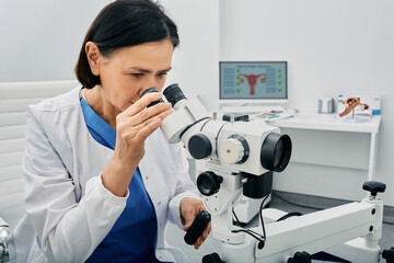 Experienced gynecologist woman sitting near colposcopy in her gynecological office. Profession of...
