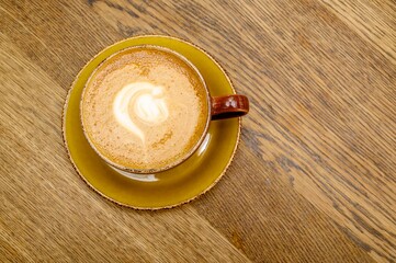 Vintage cup filled with morning fresh coffee with milk on a saucer and a picture of a heart drawn by the bartender - top view.