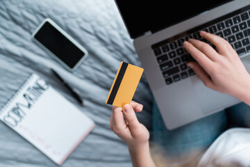 partial view of woman with credit card using laptop near blurred notebook and smartphone.