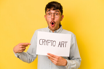 Young hispanic man holding crypto art placard isolated on yellow background pointing to the side