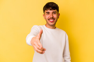 Young caucasian man isolated on yellow background stretching hand at camera in greeting gesture.