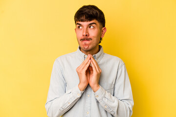 Young caucasian man isolated on yellow background holding hands in pray near mouth, feels confident.