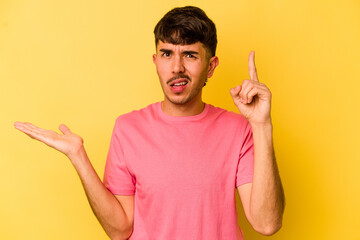 Young caucasian man isolated on yellow background holding and showing a product on hand.