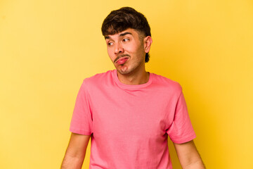 Young caucasian man isolated on yellow background shrugs shoulders and open eyes confused.