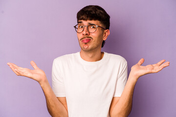 Young caucasian man isolated on purple background doubting and shrugging shoulders in questioning...