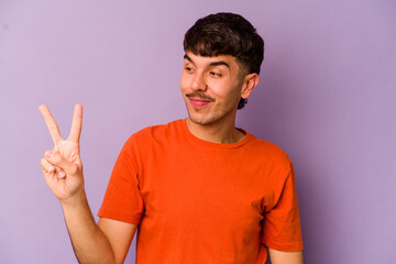 Young caucasian man isolated on purple background joyful and carefree showing a peace symbol with fingers.