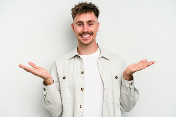 Young caucasian man isolated on white background makes scale with arms, feels happy and confident.