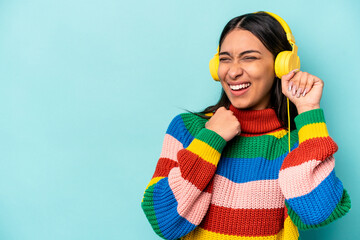 Young hispanic woman listening to music isolated on blue background raising fist after a victory, winner concept.