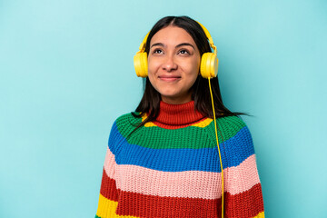 Young hispanic woman listening to music isolated on blue background dreaming of achieving goals and...