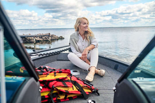 A Blonde Mature Woman In White Clothes Sitting On A Boat And Looking Dreamy