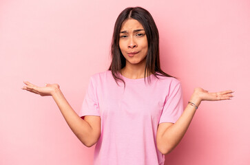 Young hispanic woman isolated on pink background confused and doubtful shrugging shoulders to hold a copy space.